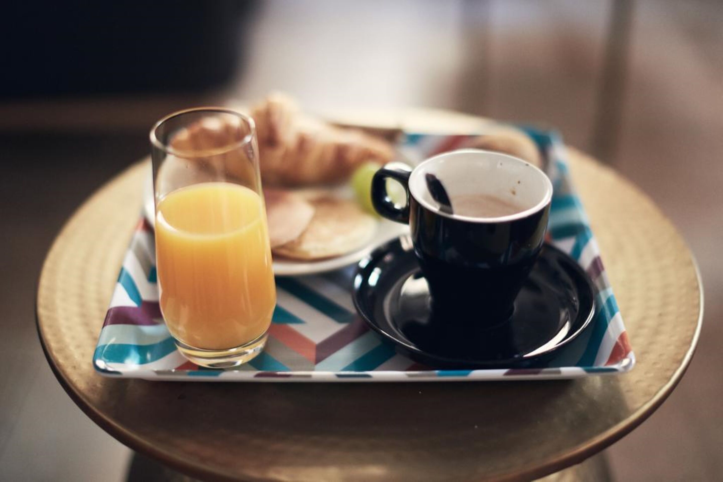 Een ontbijtplateau met een glas sinaasappelsap, een kop koffie en croissants op een tafel.