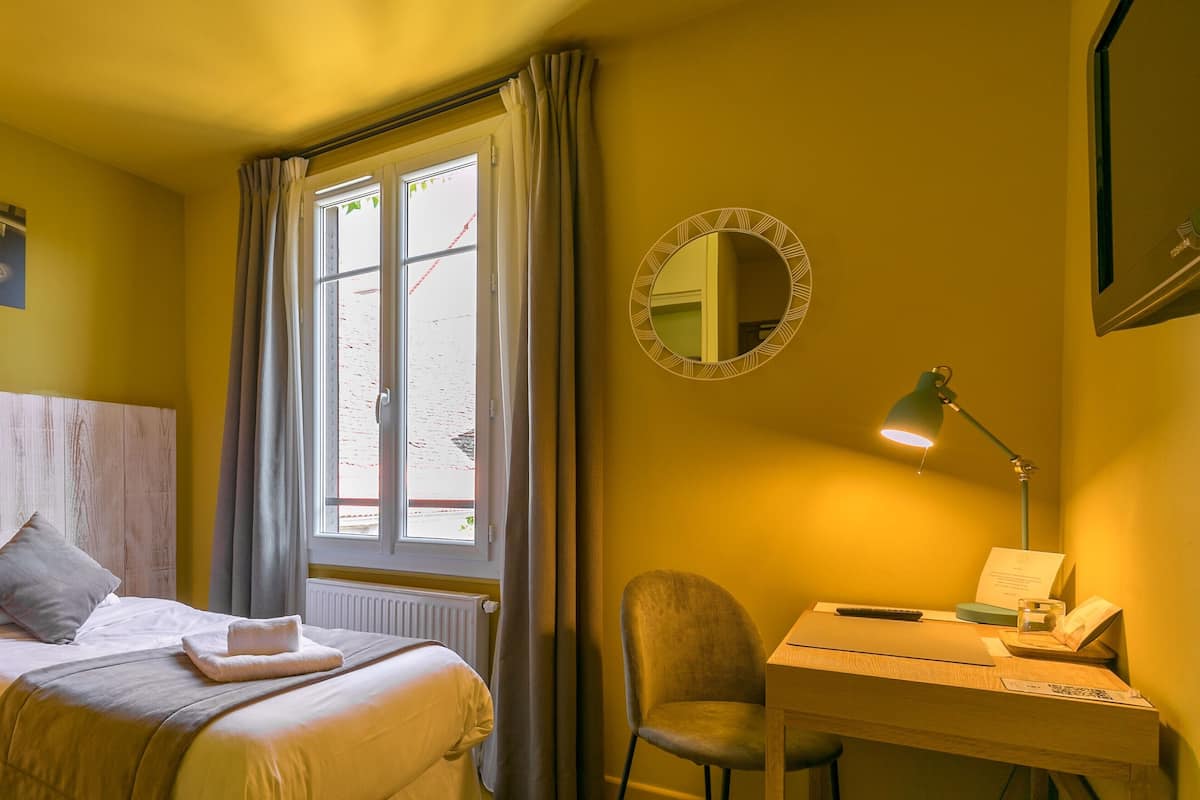 A hotel room with a bed, a desk, a chair, a window with curtains, and a mirror on the wall.