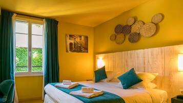 Habitación de hotel con cama, dos almohadas, una mesita de noche, lámpara, ventana con cortinas y un adorno en la pared.