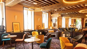 A cozy lounge area with comfortable seating, a piano, and a large mirror reflecting the room. - Le Central Boutique Hôtel (Beaune)