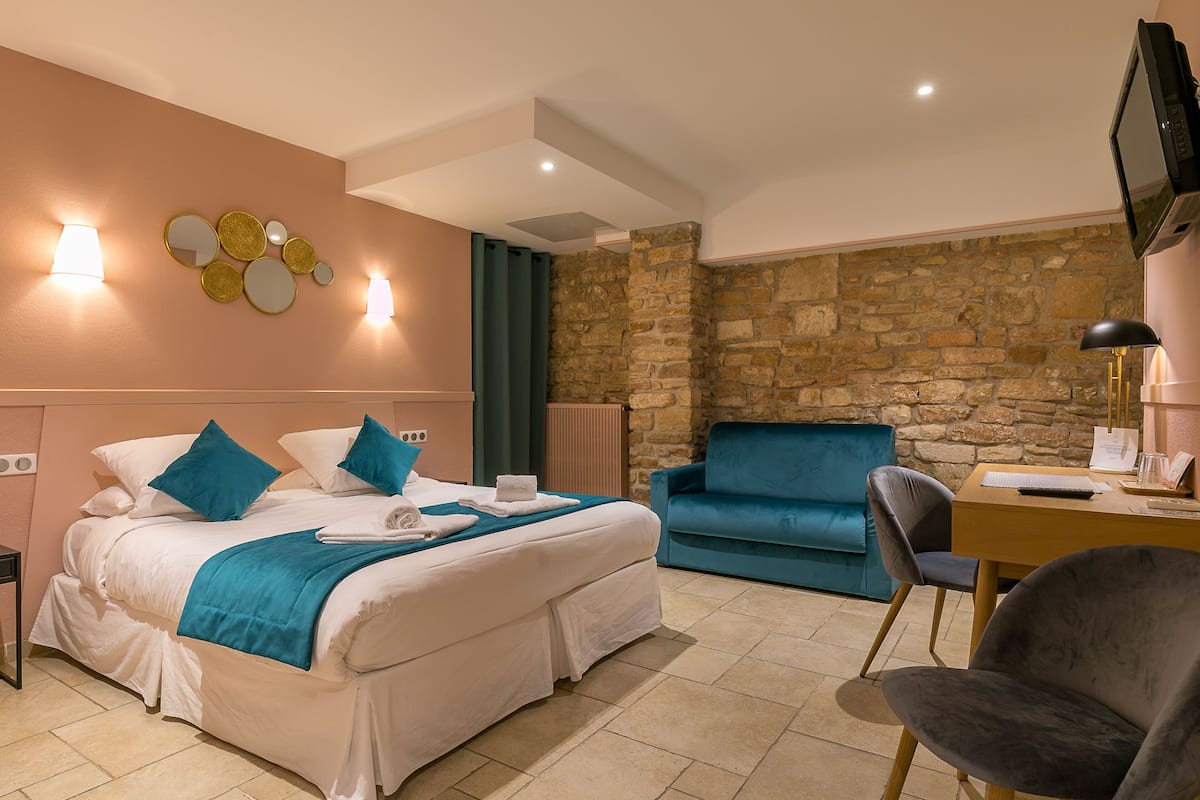A hotel room with a bed, a desk, a chair, a TV, and a stone wall.