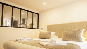 A hotel room with a large bed, two pillows, a headboard with a textured pattern, a mirror, and a window with curtains. - Le Central Boutique Hôtel (Beaune)