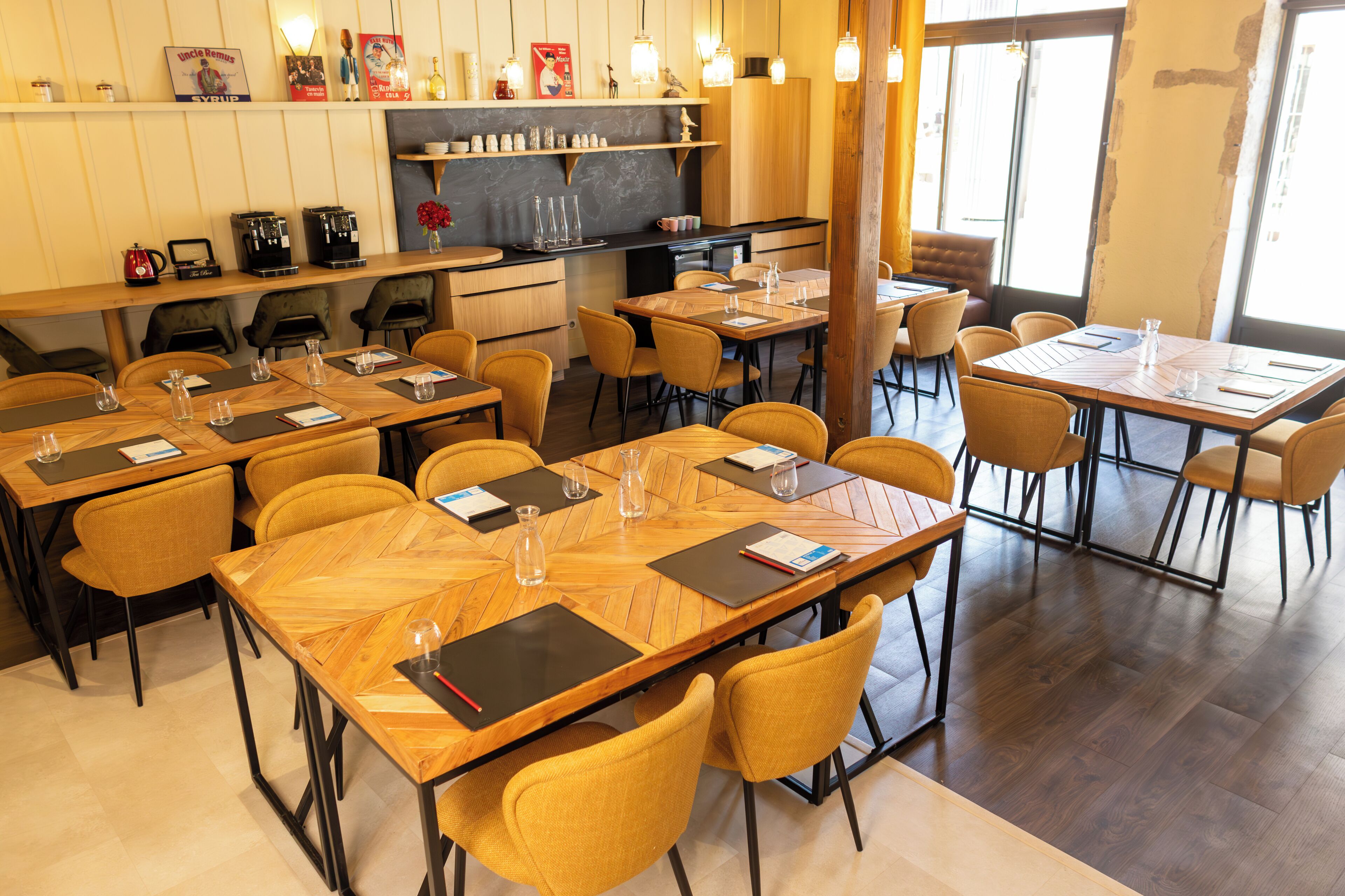 Un restaurante con varias mesas de madera y sillas amarillas, con menús, vasos y cubiertos.