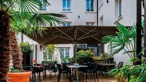 An outdoor patio area with a covered seating arrangement, potted plants, and a stone floor. - Le Central Boutique Hôtel (Beaune)