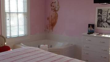 Een slaapkamer met een groot bed, een witte dressoir, een badkuip en een roze muur met een muurschildering.