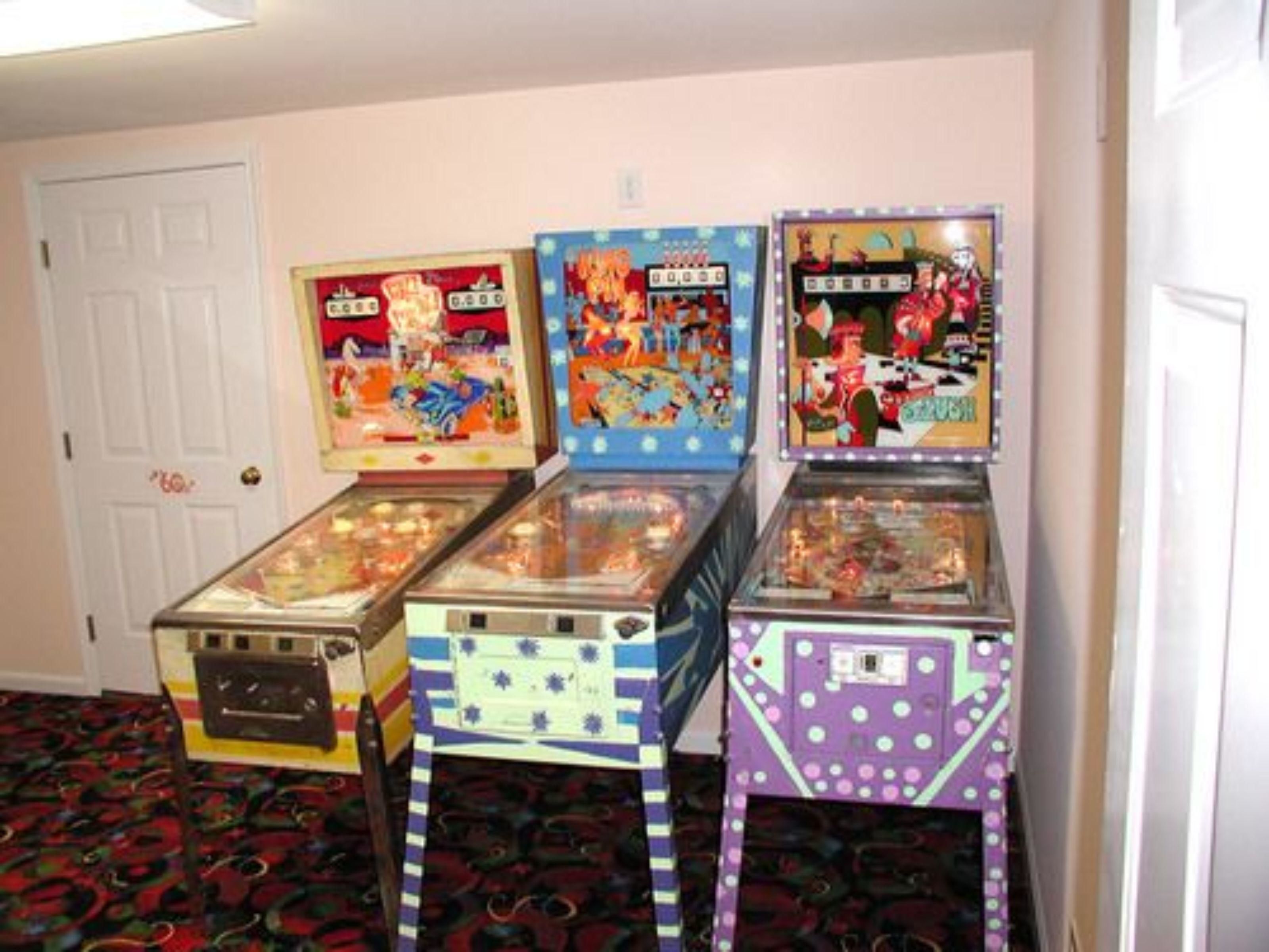 Four pinball machines in a room with patterned carpet and white walls.
