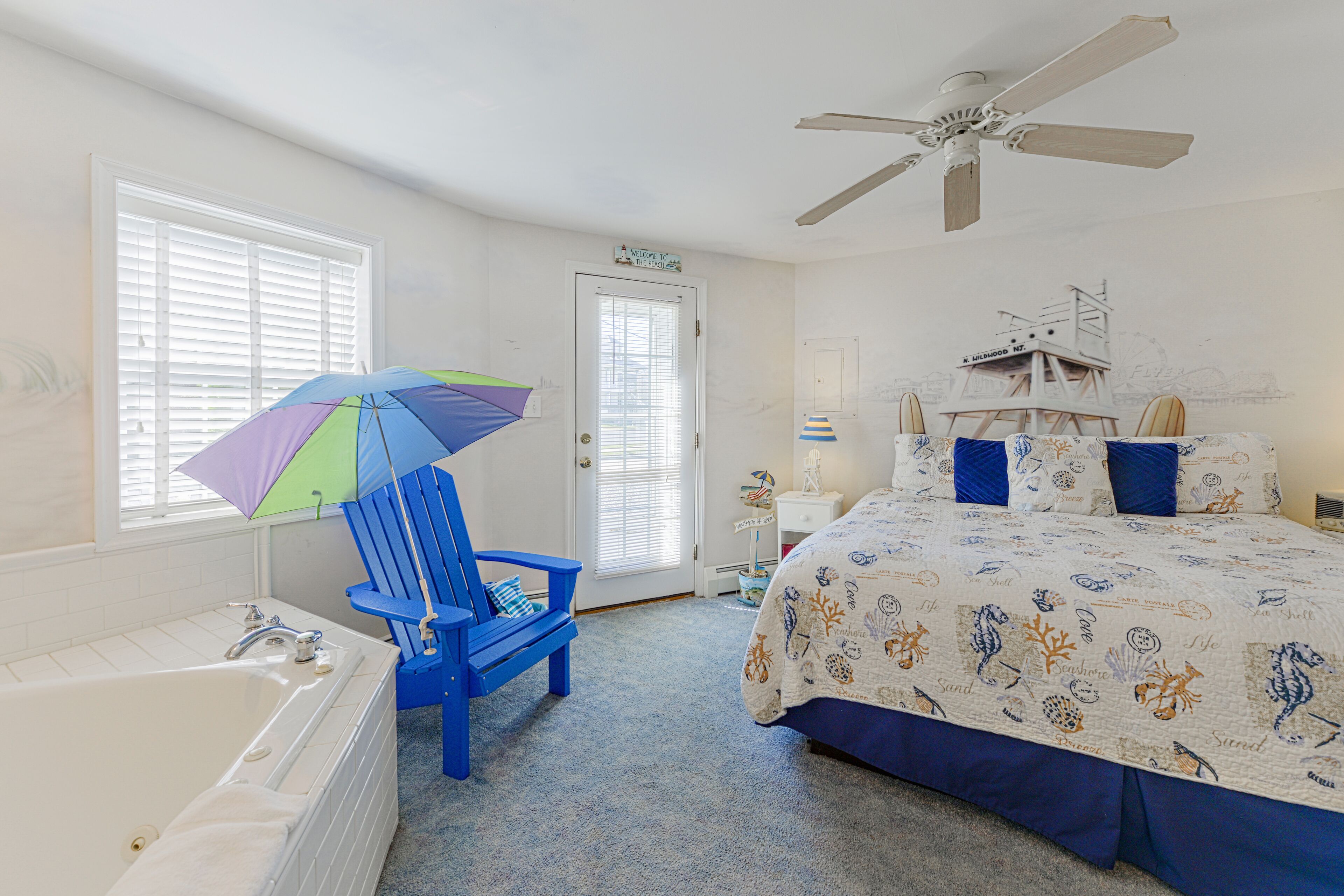 A bedroom with a bed, a blue chair, a bathtub, and a ceiling fan.