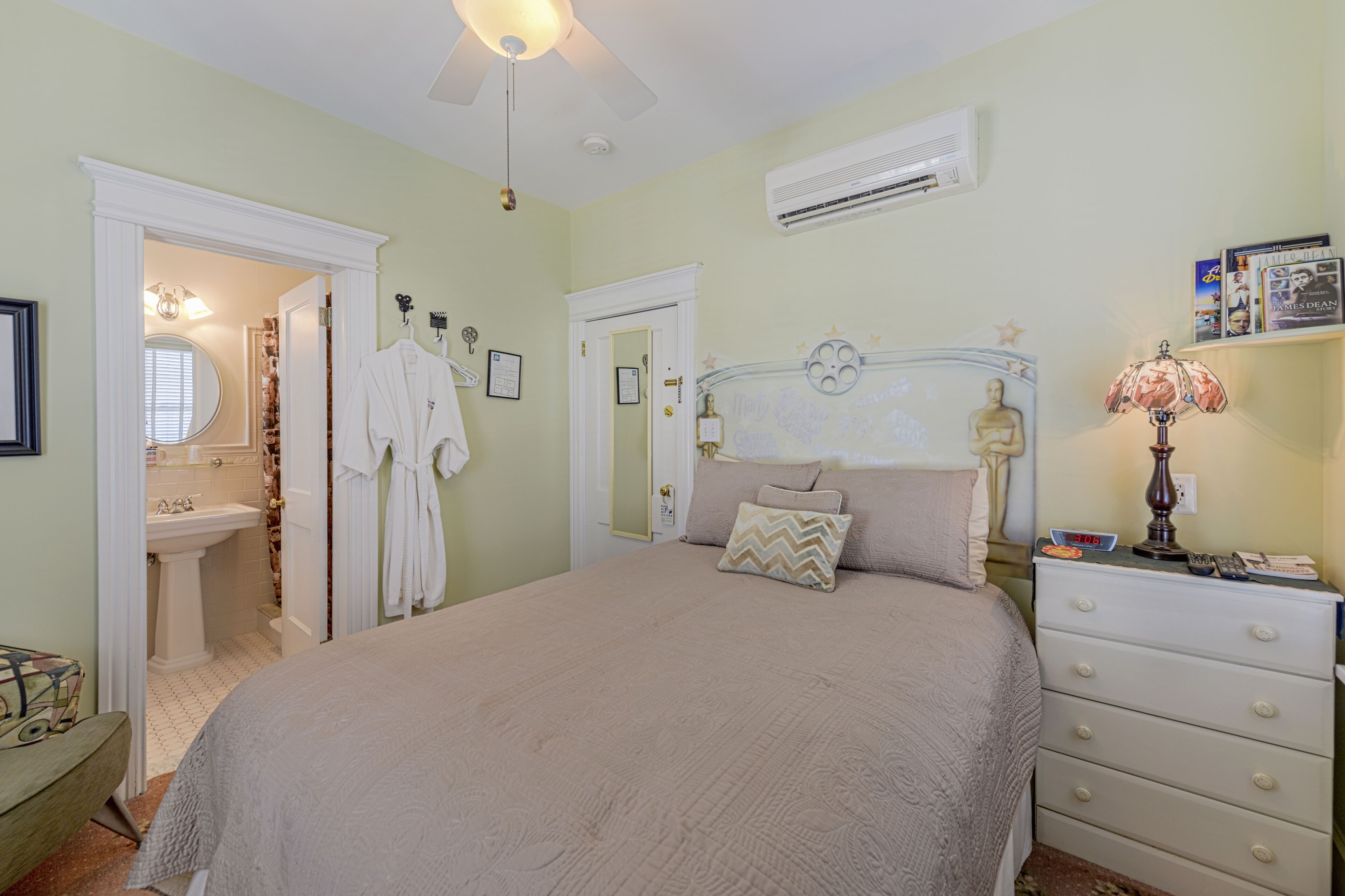 A bedroom with a bed, a dresser, a nightstand, a vanity with a mirror, and a door leading to a bathroom.