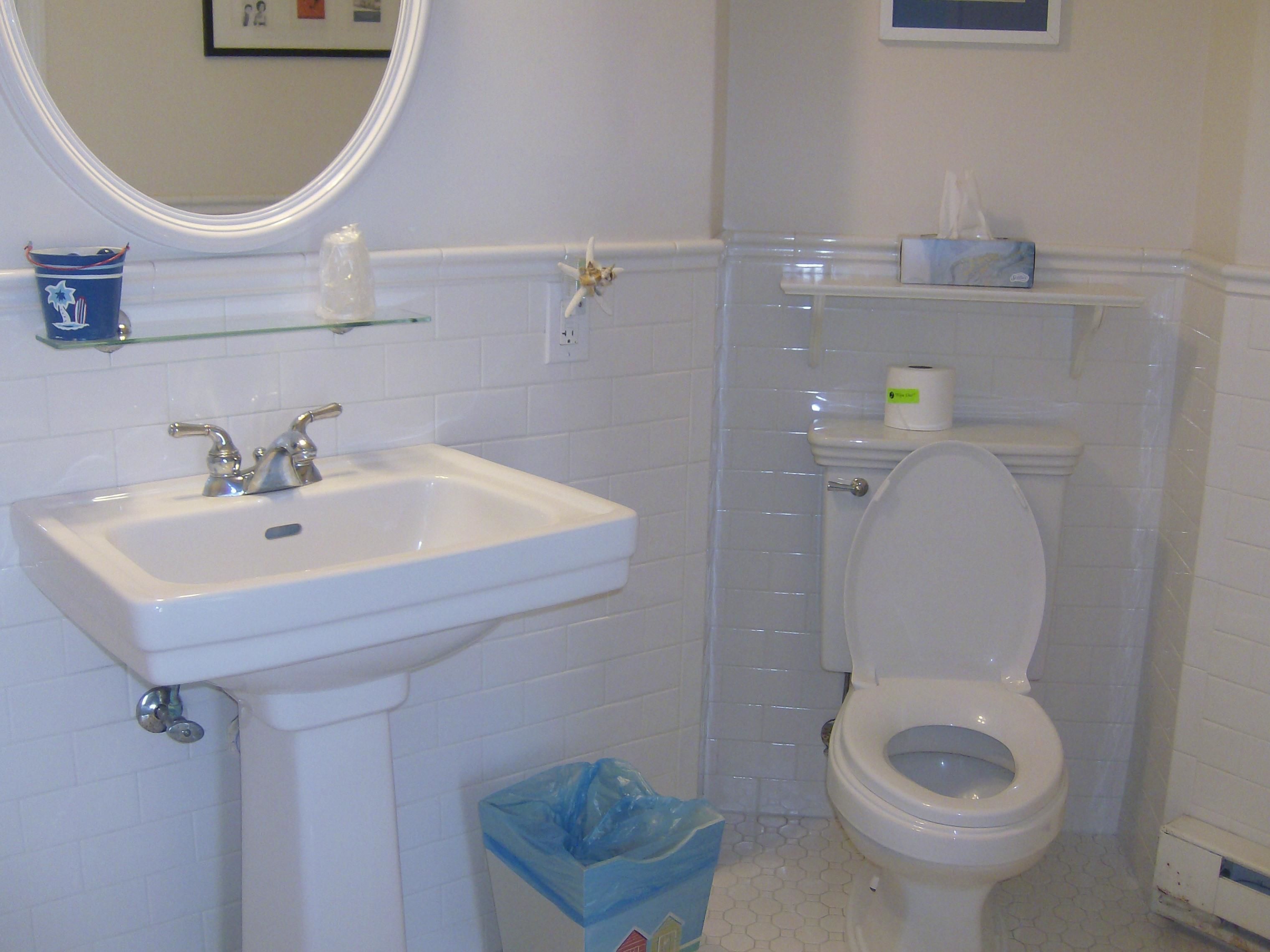 A bathroom with a white sink, toilet, and a blue trash bin.