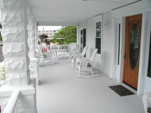 A porch with white rocking chairs and a wooden door. - Summer Nites (North Wildwood)