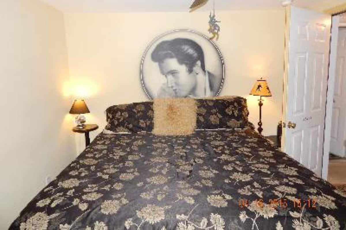 A bedroom with a bed, a ceiling fan, a wall-mounted picture, and a door.
