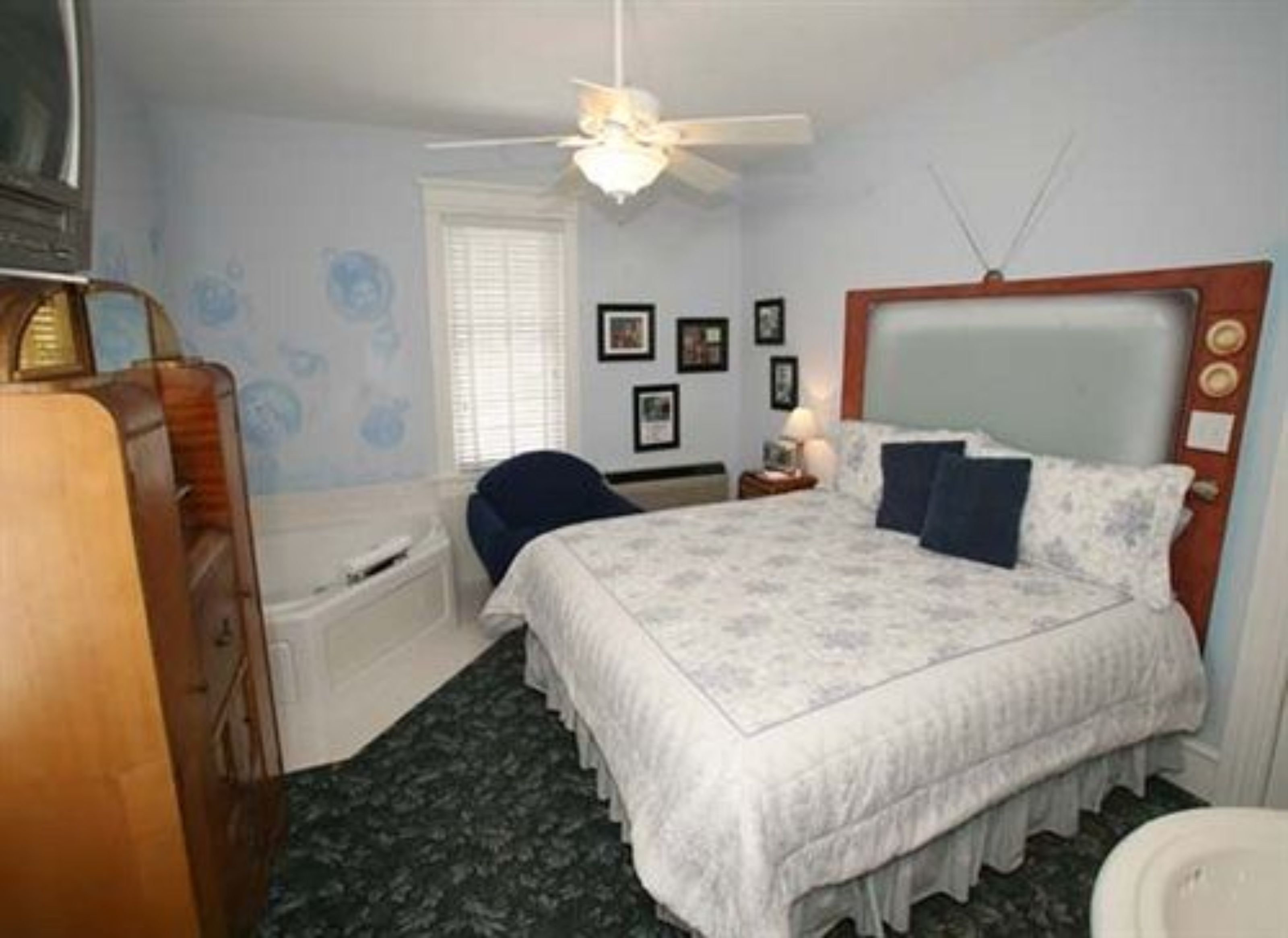 A bedroom with a bed, a desk, a chair, a ceiling fan, and a window with blinds.