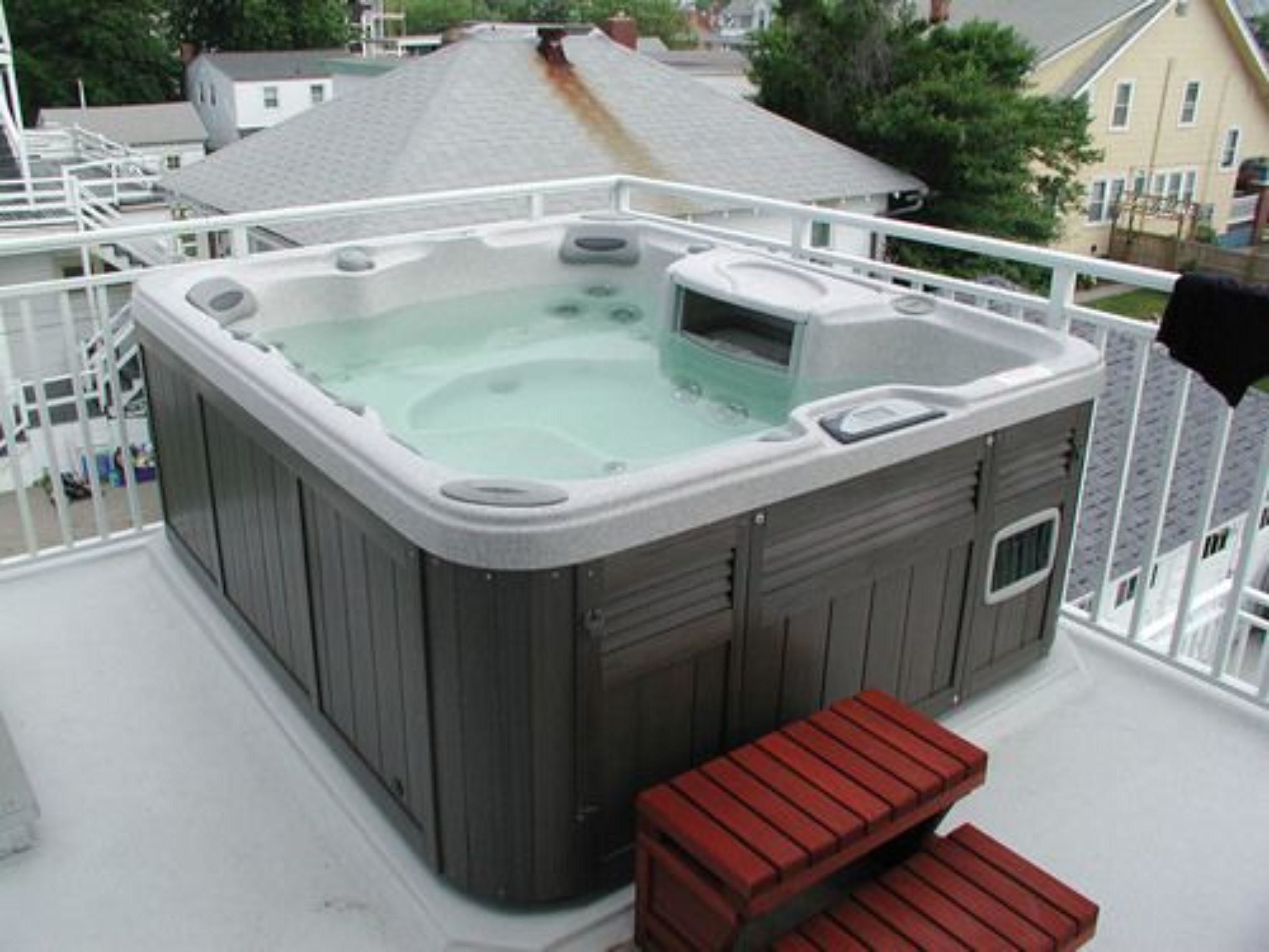 A hot tub on a balcony with a railing, a small table, and a bench.
