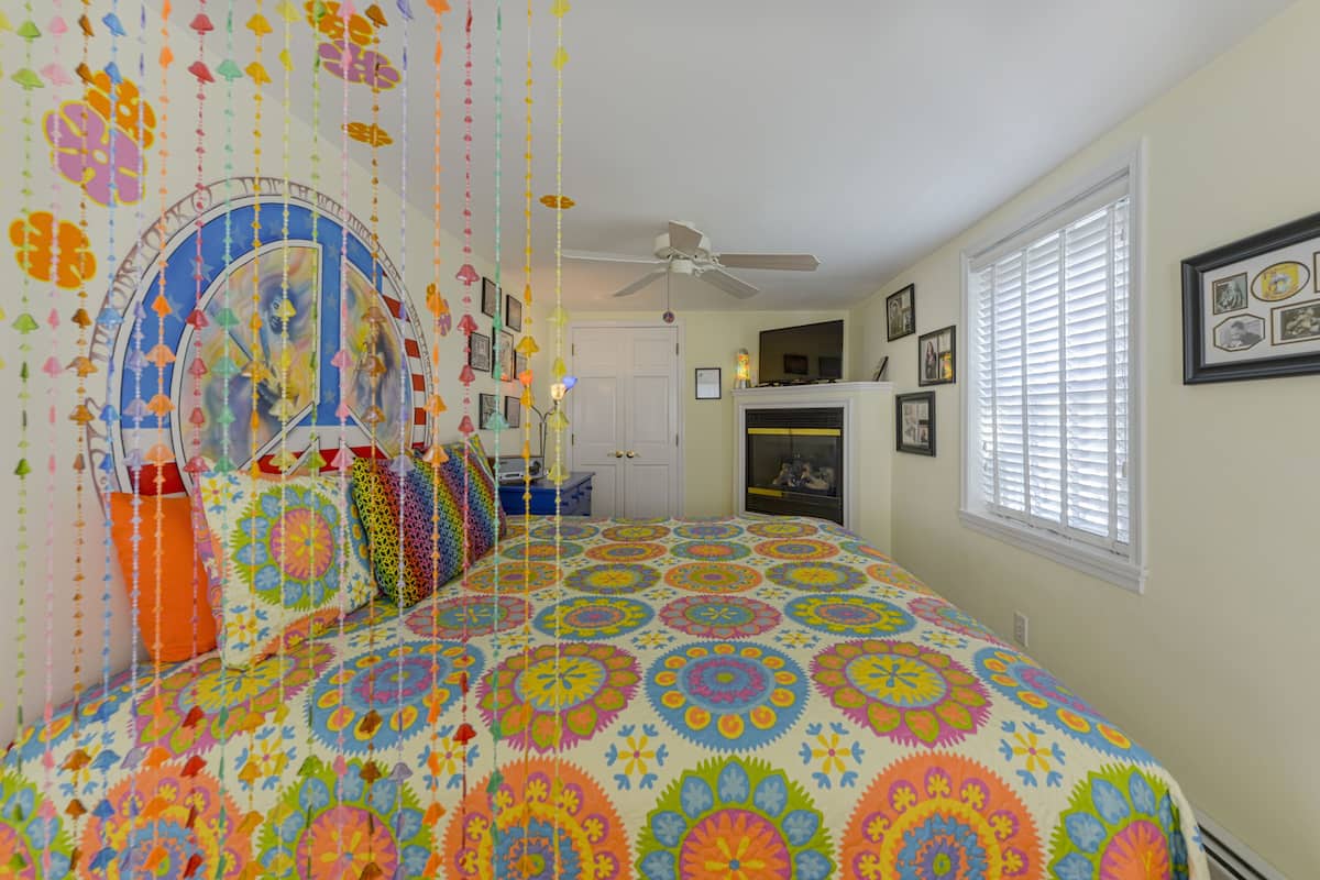 A bedroom with a colorful bedspread, a ceiling fan, and a window with blinds.