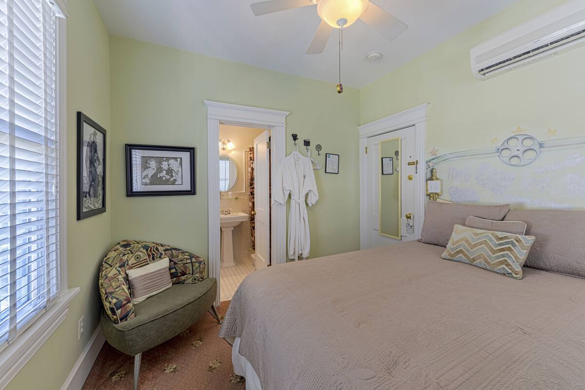 A bedroom with a bed, a chair, a vanity, and a ceiling fan.