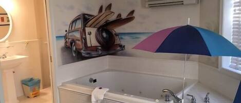 A bathroom with a large bathtub, a sink, and a mirror. There is a towel hanging on the tub, and a ceiling fan is visible.