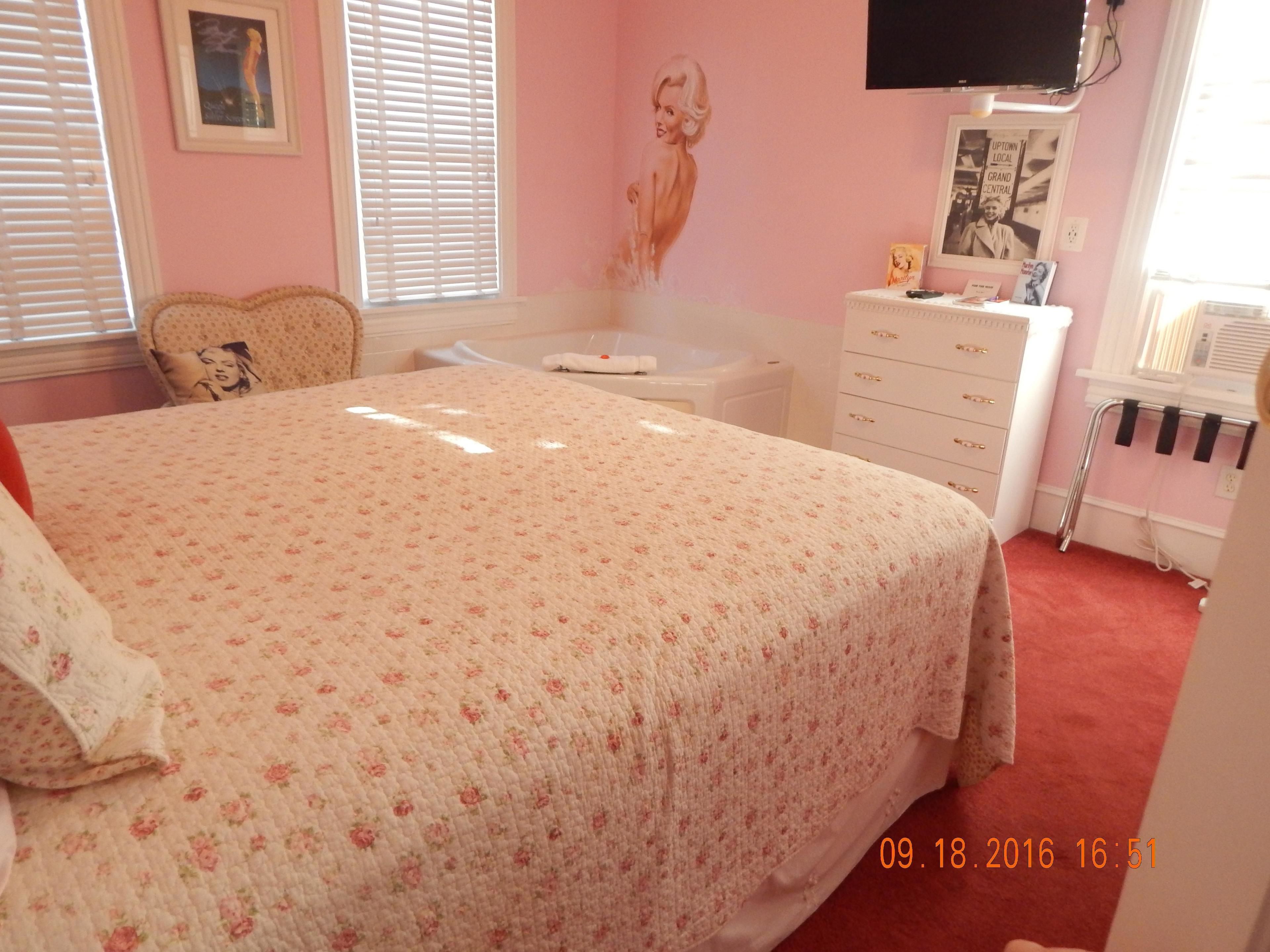 Un dormitorio con colcha estampada, cómoda, tocador, silla y televisión en la pared.