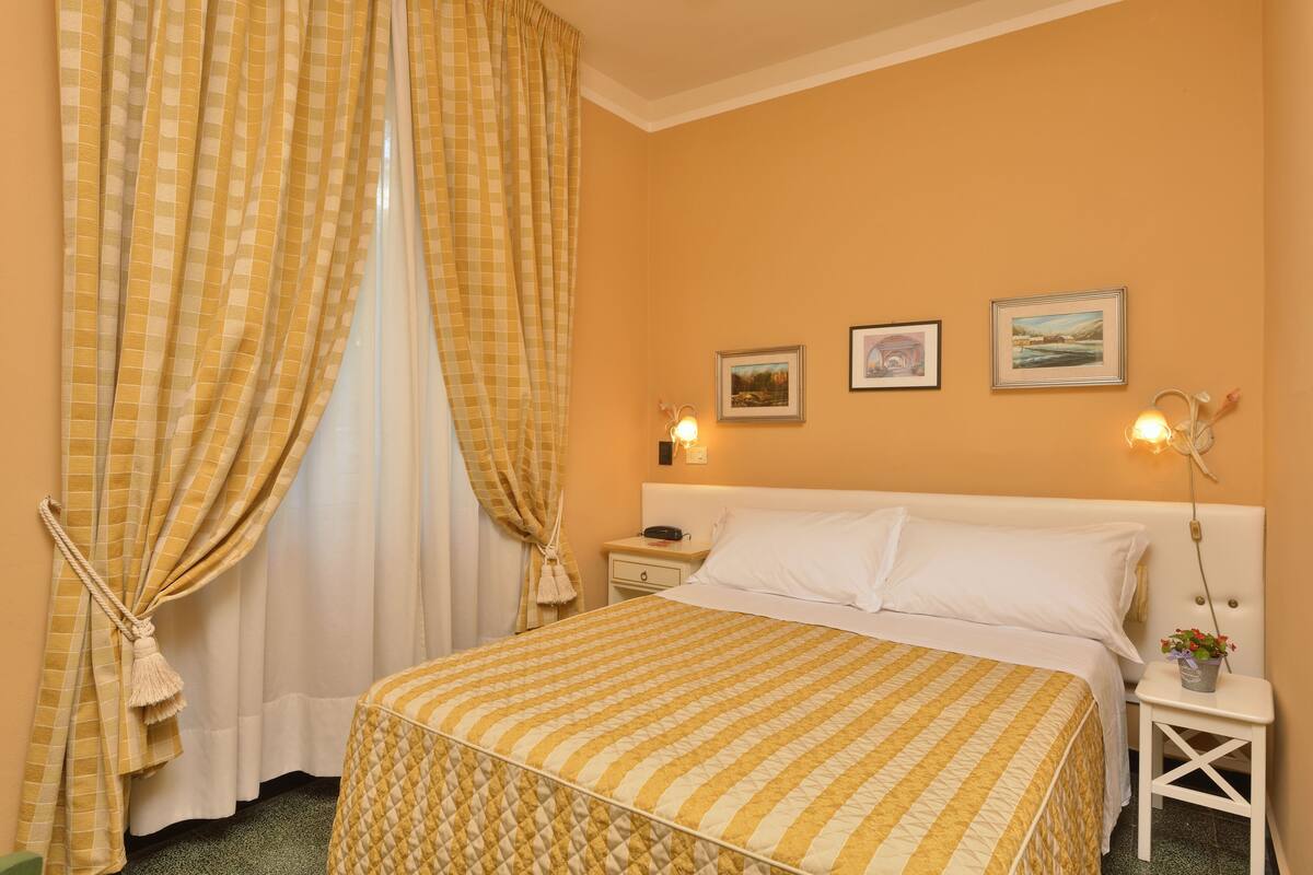 A hotel room with a bed, a nightstand, a lamp, and two framed pictures on the wall.