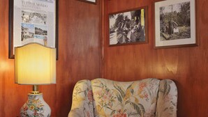 A room with a floral armchair, a wooden wall with framed pictures, and a table with a lamp. - Antica Locanda Luigina (Carrodano)
