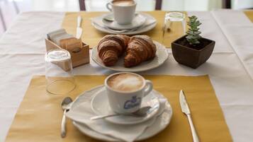 Una mesa con cruasanes, una taza de café, una pequeña planta en maceta y un vaso de agua.