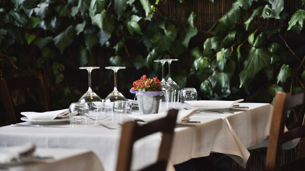 A table set for dining with a white tablecloth, clear glassware, and a small bucket with flowers. - Antica Locanda Luigina (Carrodano)