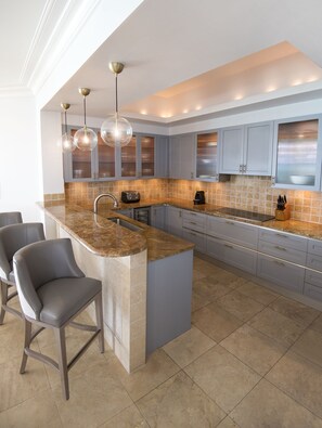 A modern kitchen with a large island, grey cabinets, and pendant lighting.