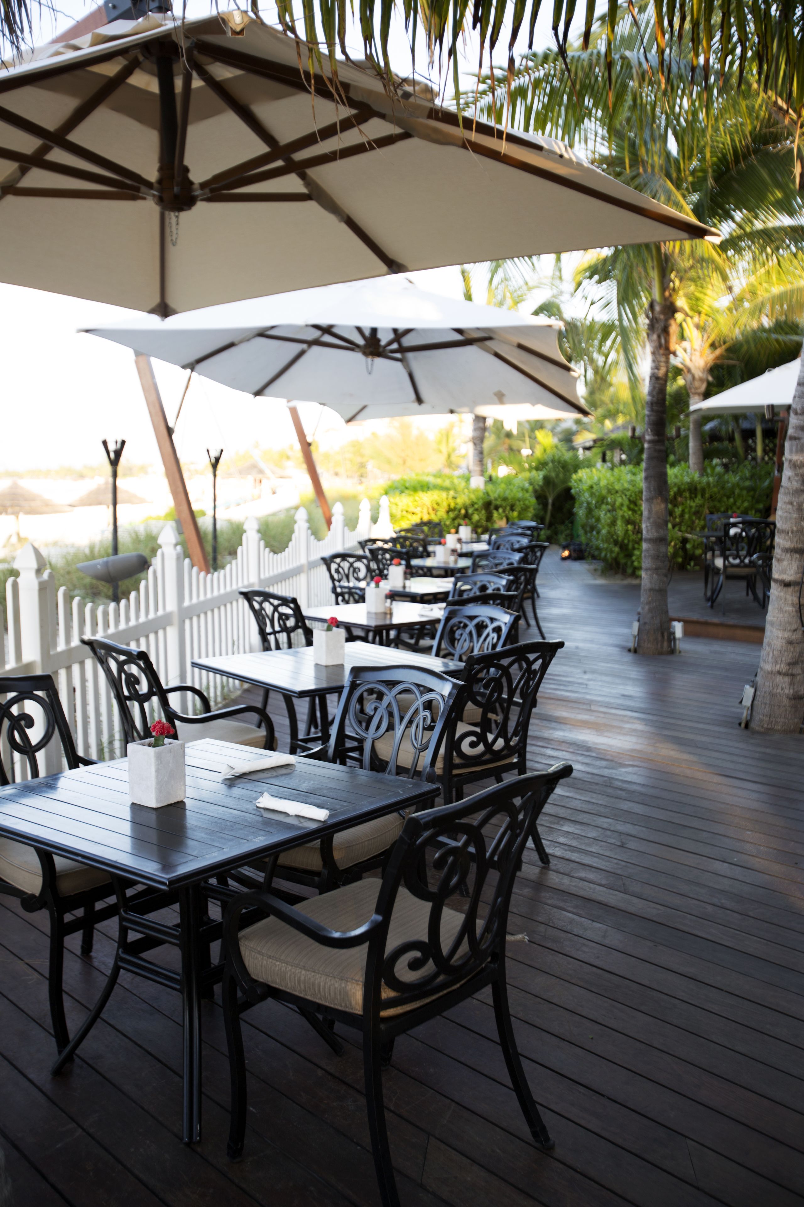 An outdoor patio with tables and chairs, umbrellas, and a white picket fence.