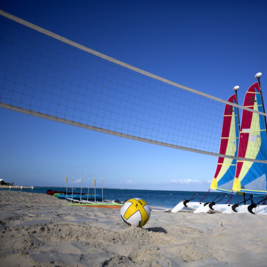 A beach volleyball net with colorful sails and a ball on the sand.