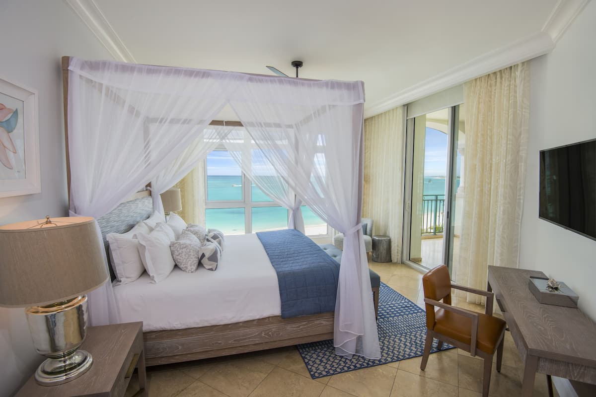 Quarto de hotel com cama, escrivaninha, cadeira, televisão e varanda com vista para o oceano.