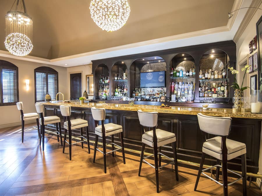 A bar area with a long counter, multiple stools, and a variety of bottles and glasses.