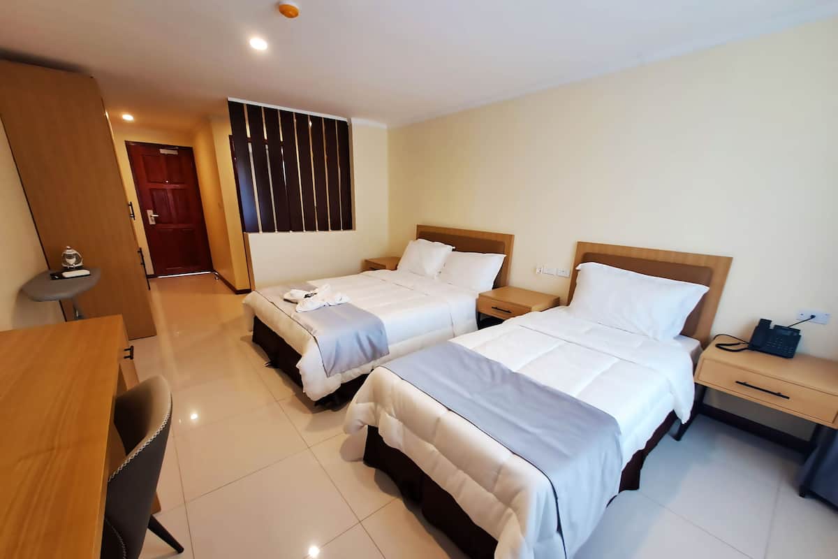 A hotel room with two beds, a desk, a chair, a small table, a wardrobe, and a bathroom door.