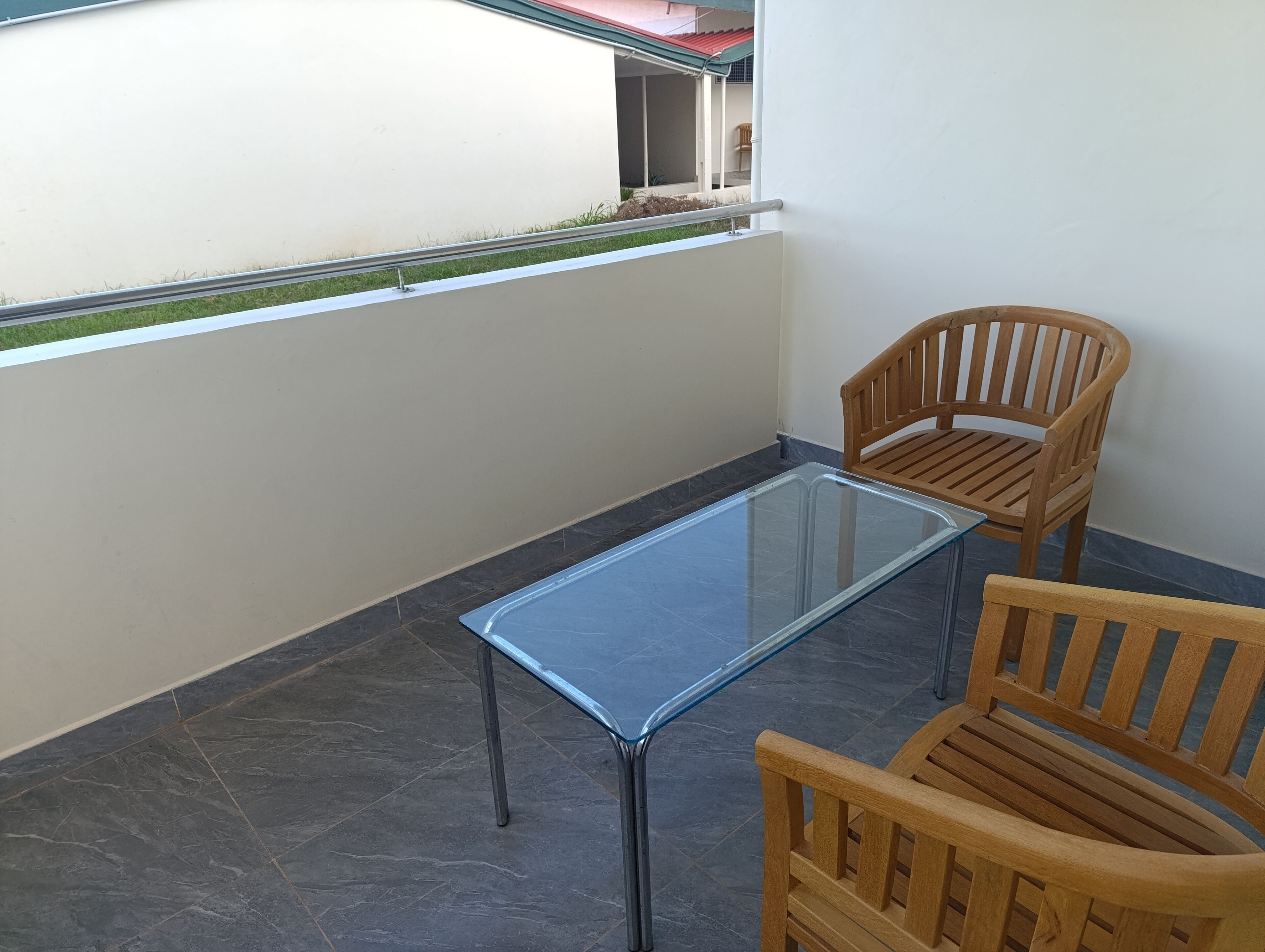 A balcony with a glass table and two wooden chairs.