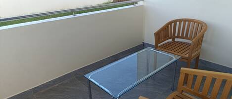 A balcony with a glass table and two wooden chairs.