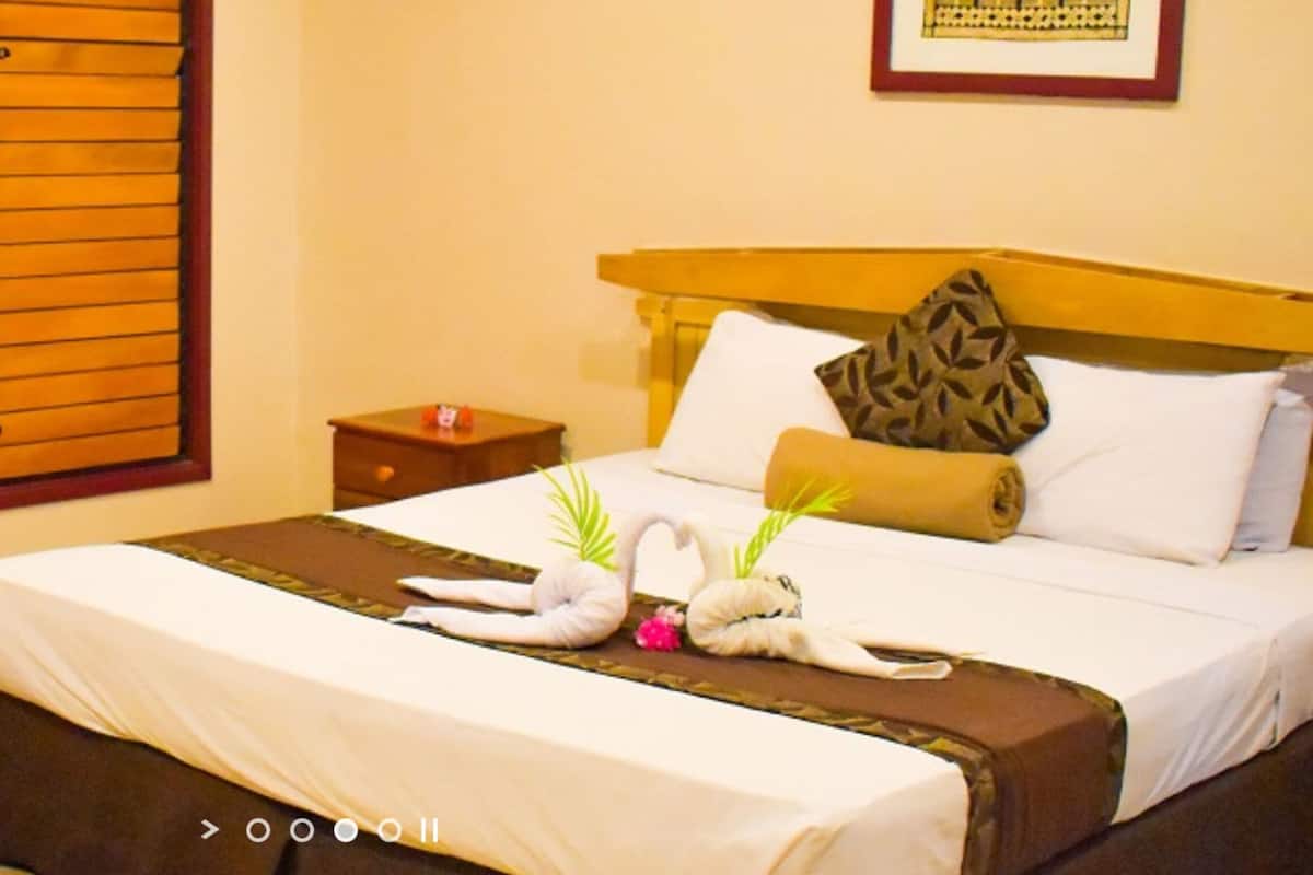 A hotel room with a bed, a brown leather sofa, a small round table, and a window with wooden blinds.