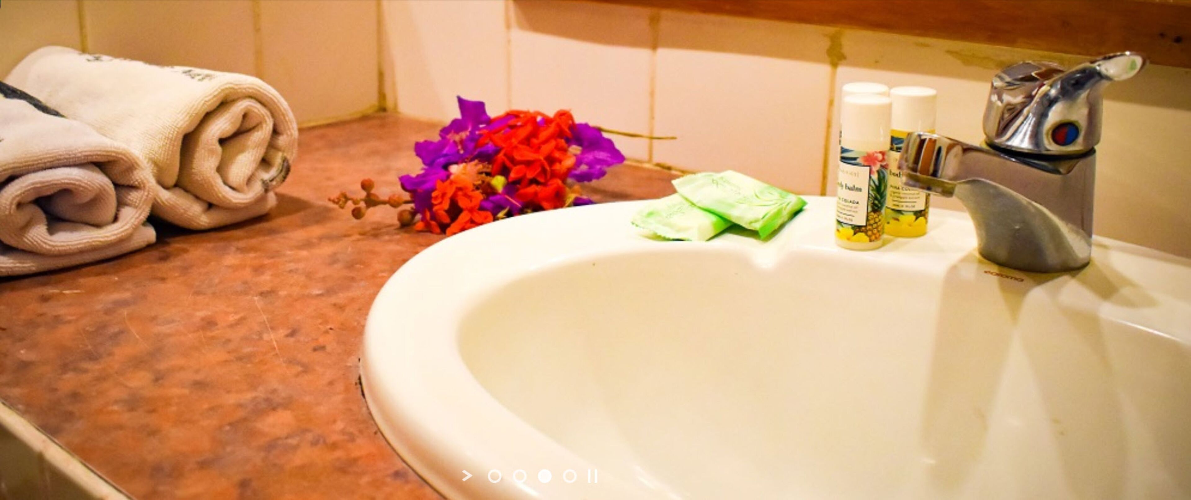 Un lavabo in bagno con articoli da toilette, un asciugamano e un bouquet di fiori.