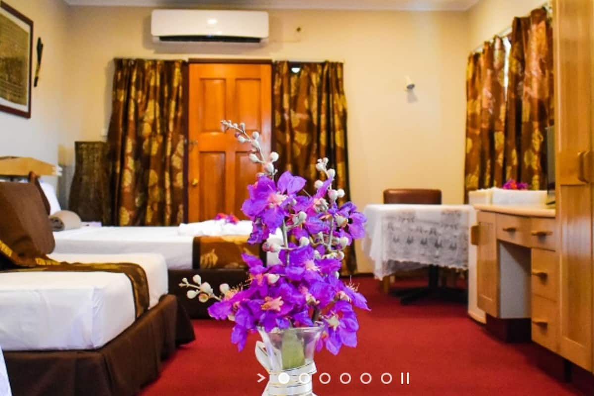 A hotel room with two beds, a desk, a chair, a vase with purple flowers, and a red carpet.