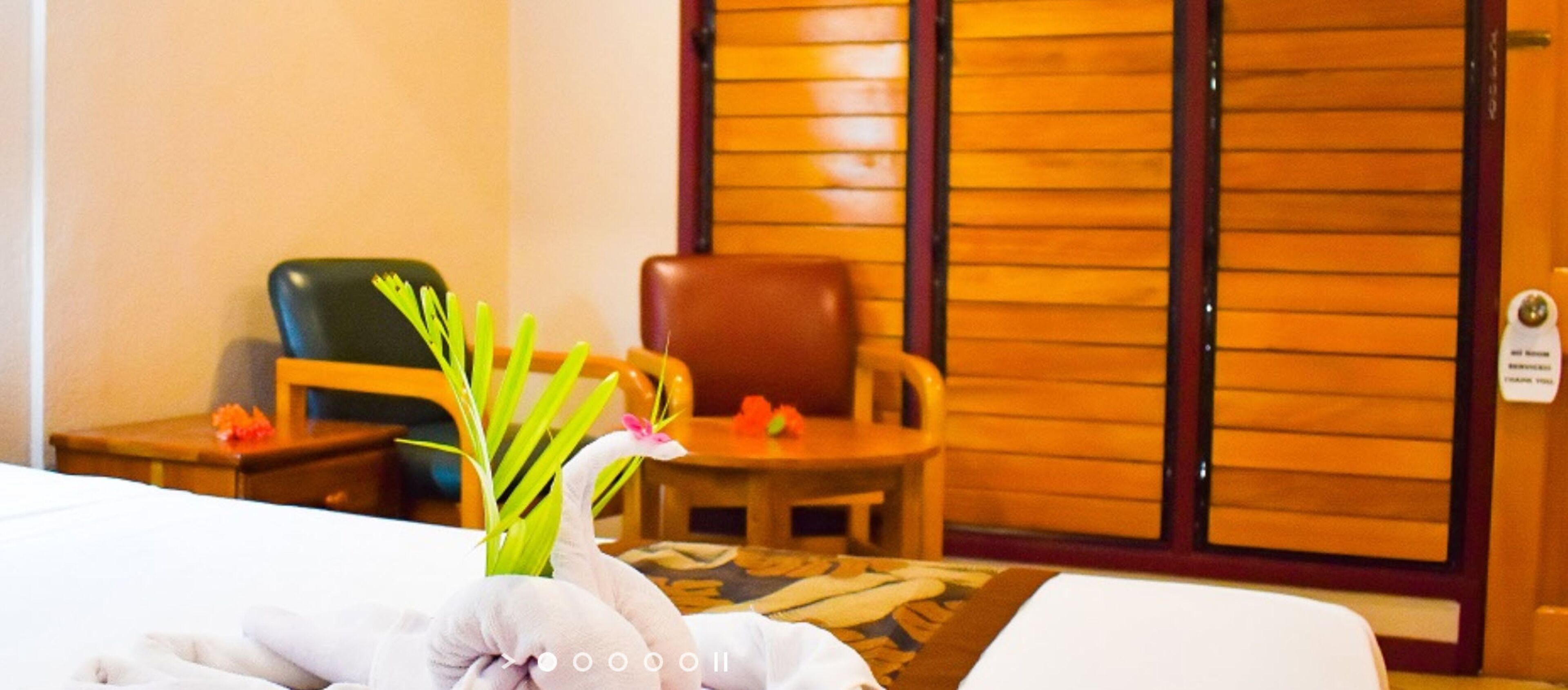 A hotel room with a bed, a wooden chair, a small table with a vase of flowers, and a wooden door.