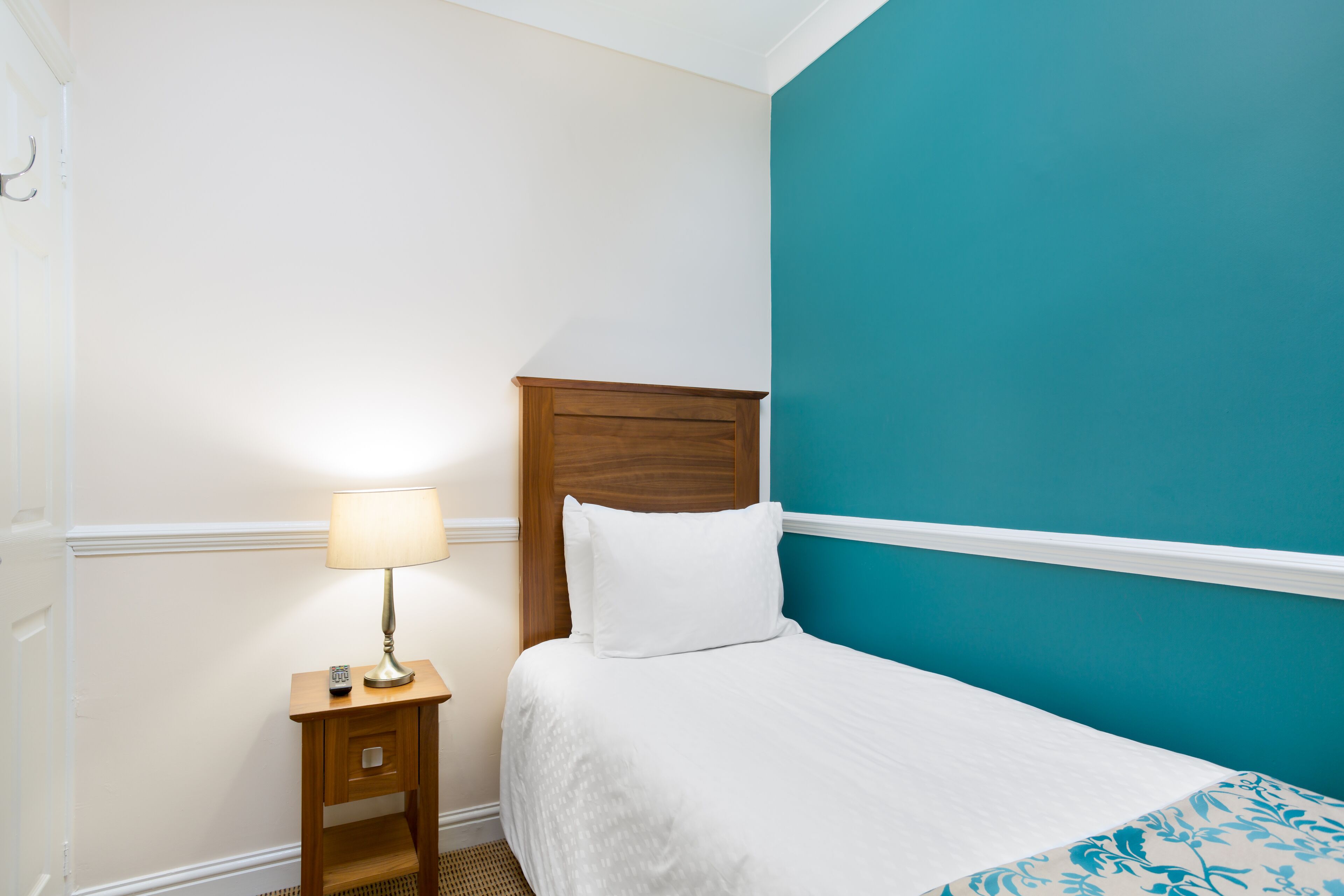 Una cama bien hecha con edredón blanco y una pared de acento color aguamarina.