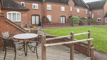 Een bakstenen gebouw met een patio, voorzien van een ronde tafel, stoelen, een houten hek en een verzorgd gazon.