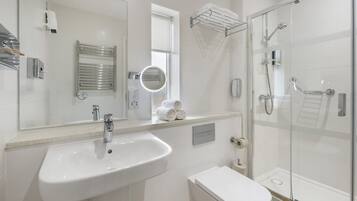 A modern bathroom with a white sink, mirror, towel rack, and glass-enclosed shower.