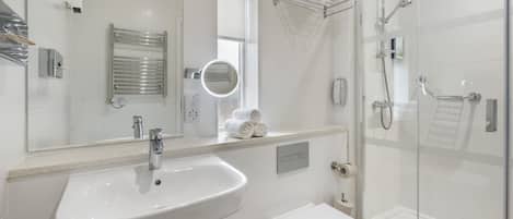 Une salle de bain moderne avec un lavabo blanc, un miroir, un porte-serviettes et une douche à parois de verre.