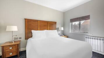 Una camera d'albergo con un letto grande, una testiera in legno, comodini con lampade, una finestra con vista e un termosifone.