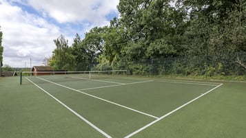 Een tennisbaan buiten met een net, omgeven door bomen en een hek.