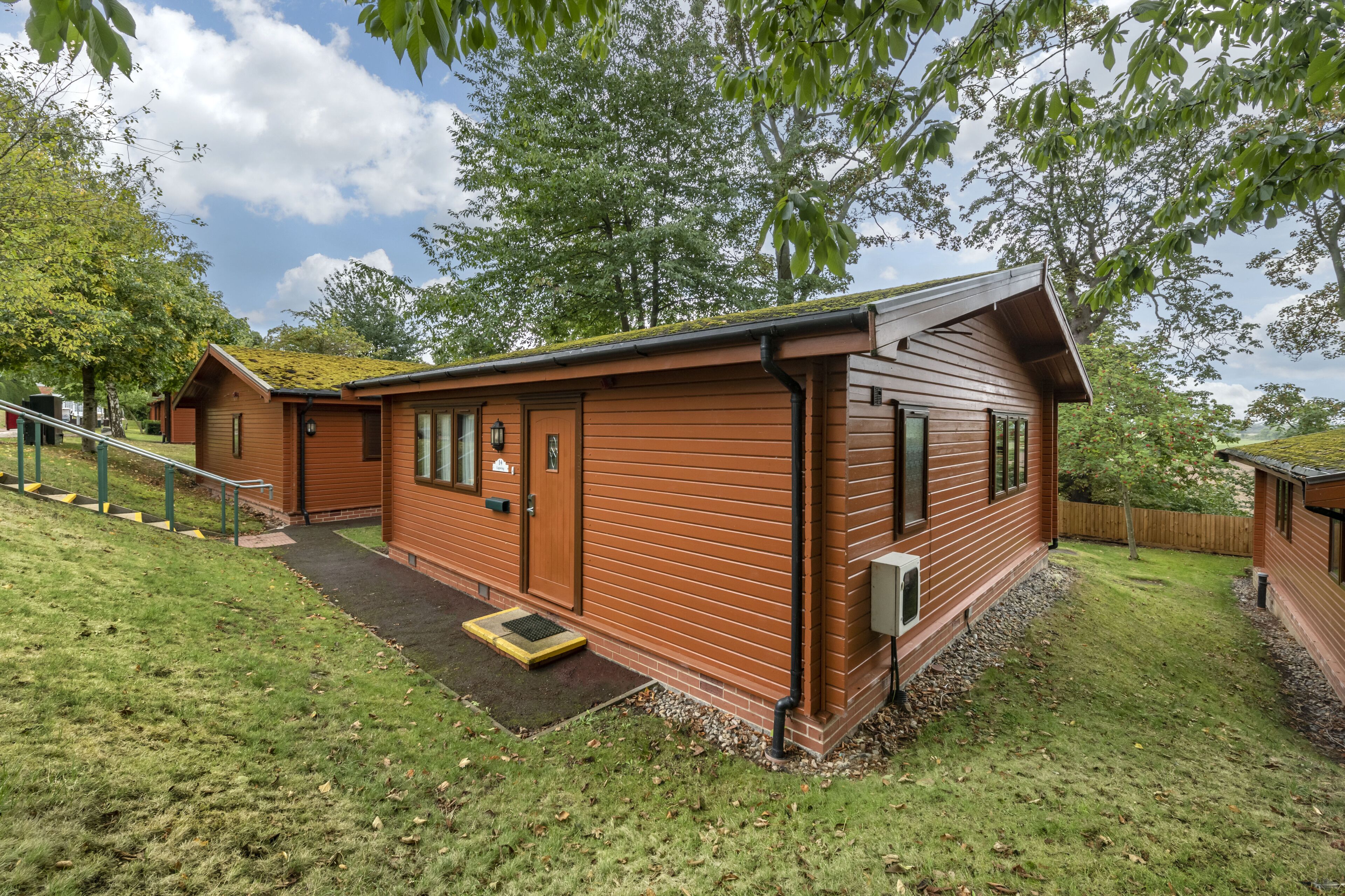 Eine Holzhütte mit Veranda, kleinem Eingang und einem Rasen.