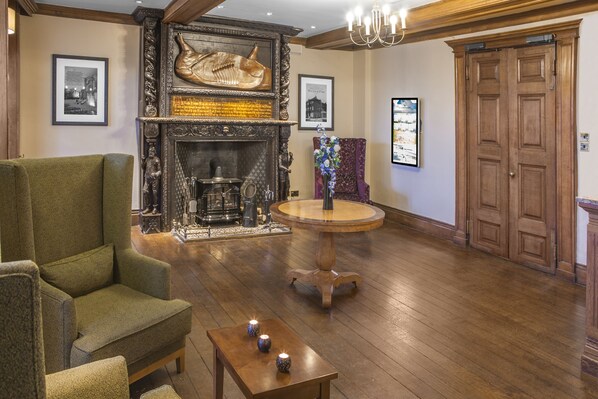 A spacious room with a fireplace, a green armchair, a round wooden table, and a large wooden door.