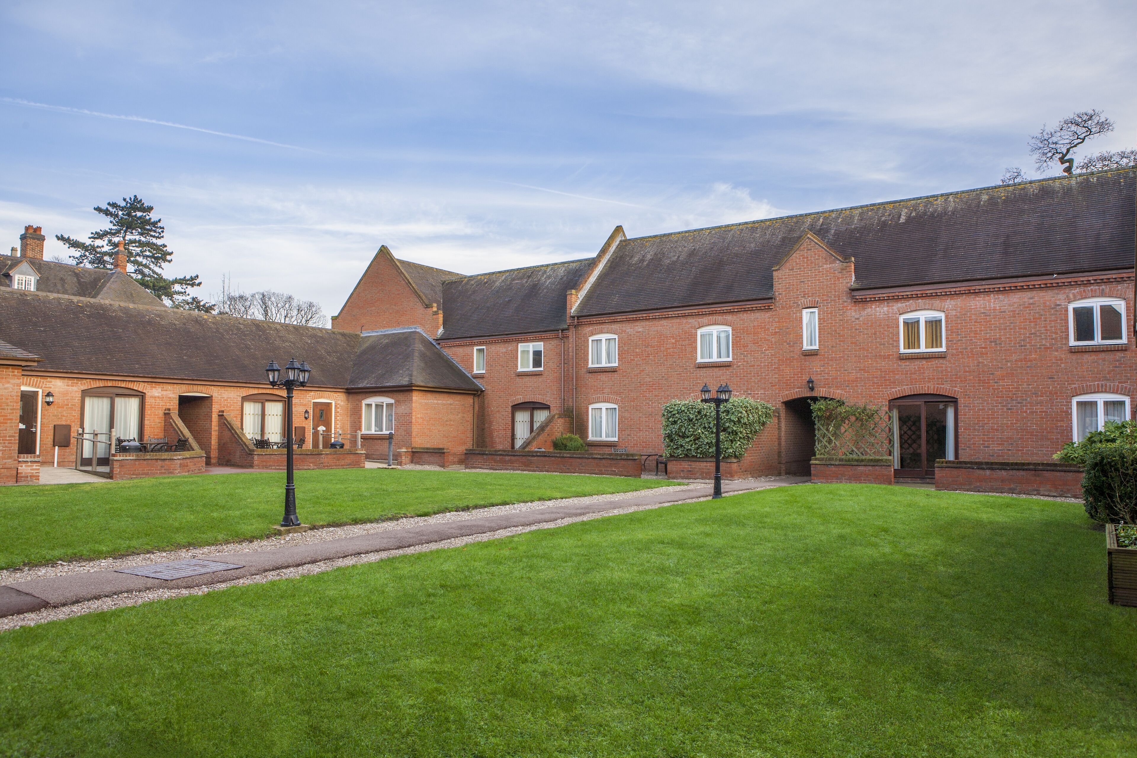 A courtyard with a brick building, a pathway, and a well-maintained lawn.