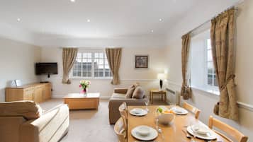 A well-lit living room with a television, seating area, and a dining table set for four.