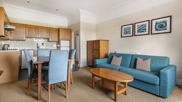 A modern living room with a blue sofa, a wooden coffee table, and a dining area with blue chairs.