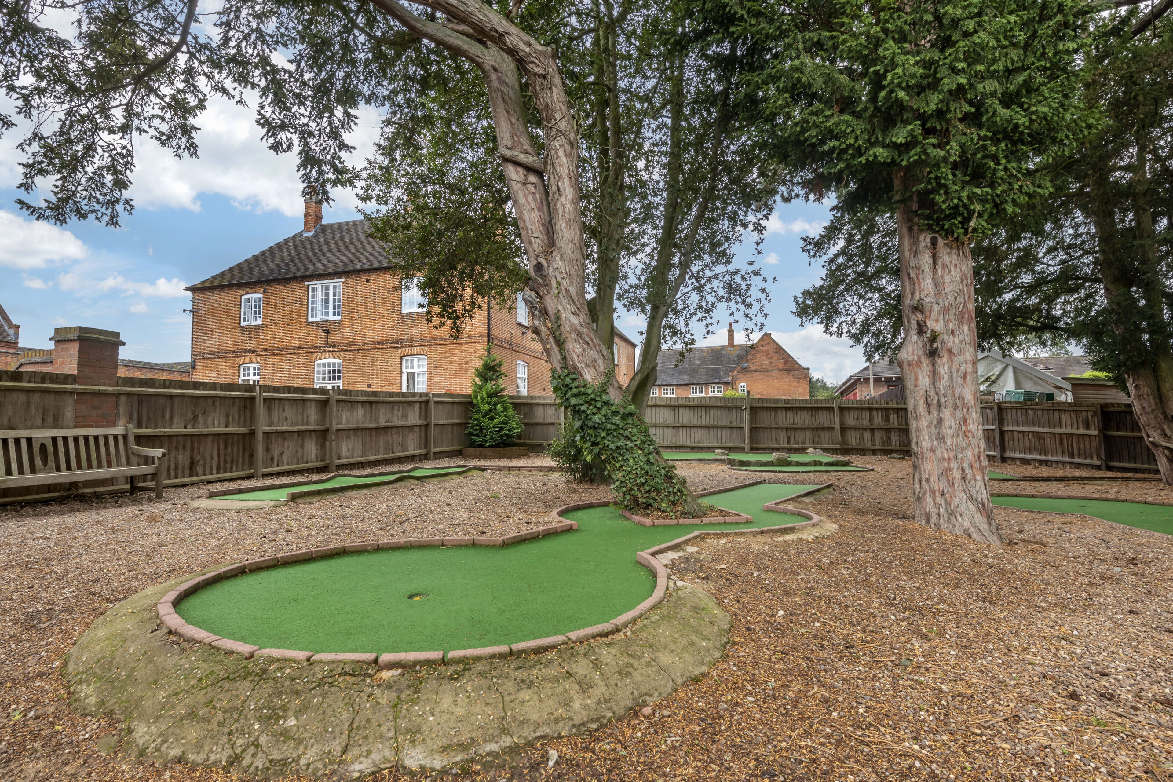 Ein Minigolfplatz mit einem grünen Putting-Bereich, umgeben von Bäumen und einem hölzernen Zaun.
