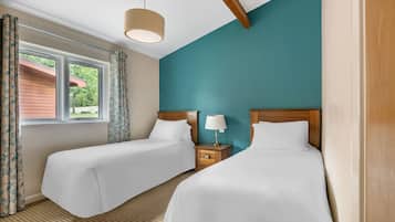 A hotel room with two beds, a window with curtains, a lamp on a bedside table, and a view of greenery outside.